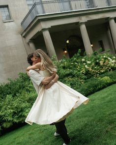 a man and woman are hugging in front of a large building with green grass on the ground