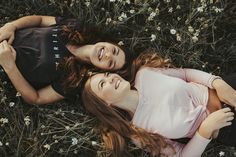 two young women laying on the ground in front of some daisies and one has her arm around another woman's shoulder