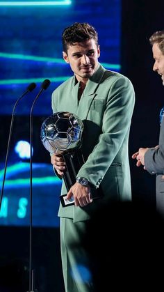 two men standing next to each other at a podium holding soccer balls in their hands