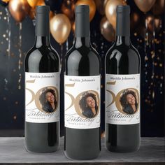 three bottles of red wine sitting next to each other on a table with balloons in the background