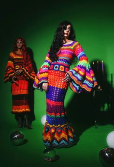 a woman in a colorful dress standing next to two other women wearing crocheted clothing