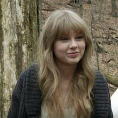 a woman with long blonde hair standing next to a tree