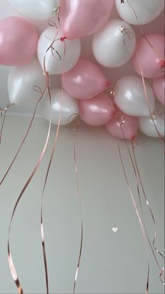 pink and white balloons floating in the air with streamers attached to it's ceiling