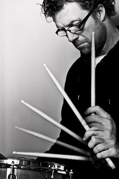 a man with glasses holding drums sticks in front of his face and looking at the camera