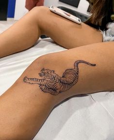 a woman laying in bed with a tattoo on her leg that has a tiger on it