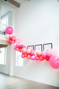 a long line of pink and orange balloons hanging from the side of a white wall