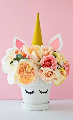 a white cup with flowers and a unicorn face on it's head, sitting in front of a pink wall