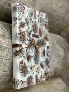 a square clock with pine cones and leaves on it