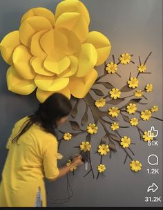 a woman is working on a paper flower wall decoration with yellow flowers in the background