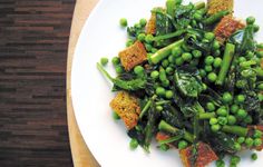 a white plate topped with green vegetables and breaded croutons on top of a wooden table