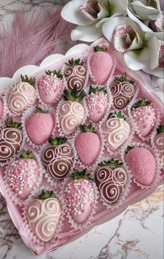 chocolate covered strawberries are arranged in a heart shaped box on a marble surface next to flowers