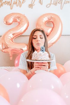 a woman sitting in front of balloons and holding a plate with a cake on it