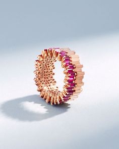 a gold ring with pink and red stones on the inside, sitting on a white surface