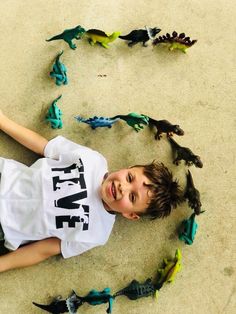 a young boy laying on the ground surrounded by toy dinosaurs