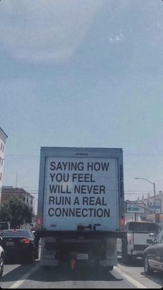 a large truck driving down a street next to tall buildings and traffic cones with words written on the back