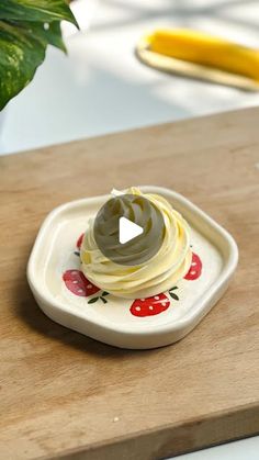 a small white plate topped with whipped cream on top of a wooden table next to a potted plant