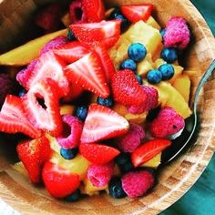 a wooden bowl filled with fresh fruit on top of a blue table next to a fork