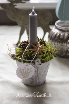 a small candle is sitting in a pot with moss and pine cones on the table