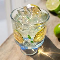 a glass filled with ice and lemons on top of a wooden table next to limes