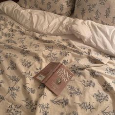 a book is laying on top of a bed with white sheets and blue floral print