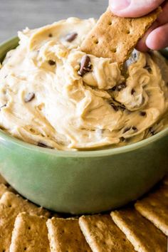 a hand dipping a cracker into a bowl of peanut butter and chocolate chip dip