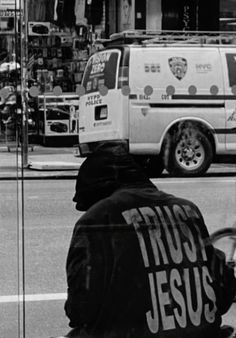 a man sitting on the side of a road next to a van and another person riding a bike