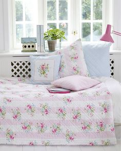 a bed covered in pink and white flowers next to a window with two windows behind it