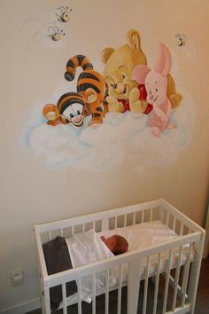 a baby sleeping in a crib next to winnie the pooh wall decal