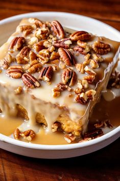 a white plate topped with cake covered in frosting and pecan toppings on top of a wooden table