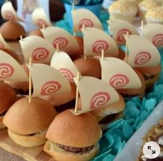 small sandwiches with sailboats on them sitting on a wooden tray next to cupcakes