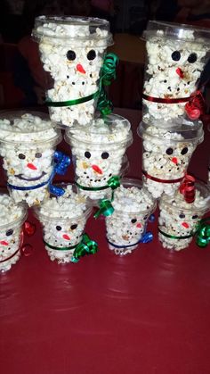 there are many snowmen made out of popcorn in plastic cups on the red table