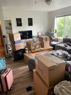 a living room filled with lots of boxes next to a couch and television on top of a hard wood floor