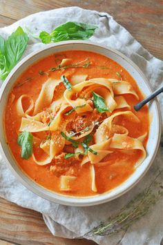 a white bowl filled with pasta and sauce on top of a wooden table next to a napkin