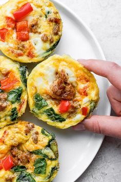 four breakfast muffins with sausage, spinach and tomatoes on a white plate