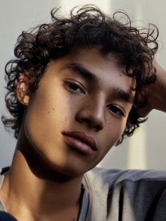 a young man with curly hair is looking at the camera while holding his hand on his head