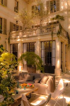 a living room filled with furniture next to a tall white building surrounded by greenery