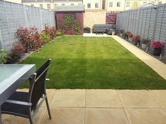 a small backyard with grass and flowers in the back yard, next to a patio