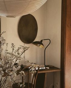 a table with a lamp and some flowers on it in front of a round mirror