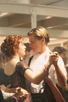 a man and woman dancing together at a party with other people in the back ground