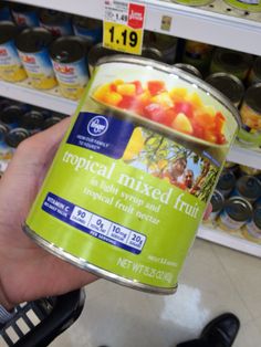 a hand holding a can of tropical mixed fruit in a grocery store's aisle