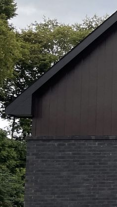 a clock on the side of a black building with trees in the backgroud