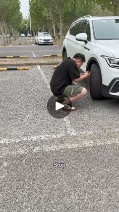 a man kneeling down next to a white car in a parking lot with another man fixing the tire