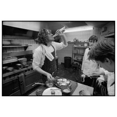 black and white photograph of three people cooking in a kitchen with one woman drinking from a bottle