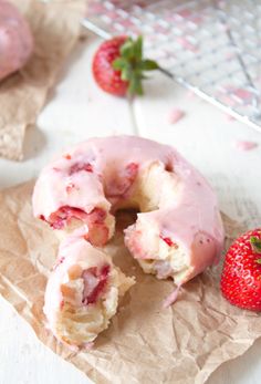 a donut with pink icing and strawberries on top of it sitting on wax paper