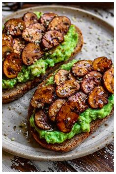 two pieces of toast with avocado and mushrooms on it, sitting on a plate