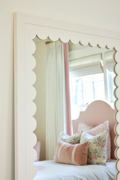 a white bed sitting next to a window in a bedroom under a large framed mirror