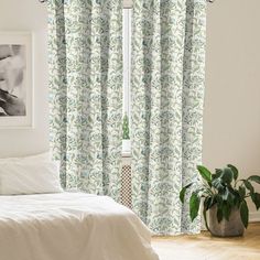 a white bed sitting under a window next to a green plant in front of it