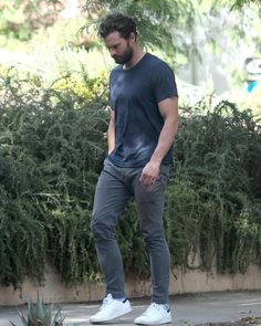 a man standing on top of a skateboard in front of a hedged area