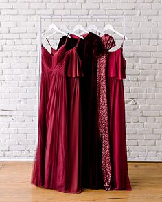 three bridesmaid dresses hanging up in front of a white brick wall and wooden floor