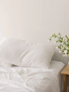 a bed with white sheets and pillows on top of it next to a wooden table